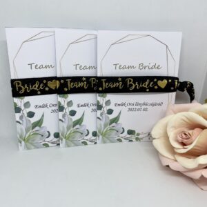 TEAM BRIDE fekete, arany felirattal, fehér virágos kártyával lánybúcsús karkötő